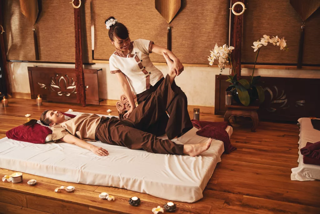 Joyful masseuse raising left leg of female during massage